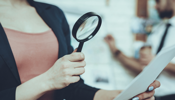 focussed image of woman holding a magnifying glass pointed towards a paper she is holding showcasing background screening trends