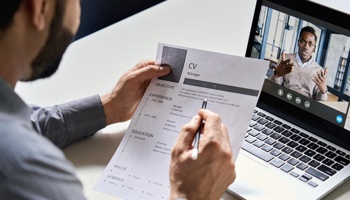 man holding a pen and a CV with a young black man on a zoom call job interview style when hiring remotely
