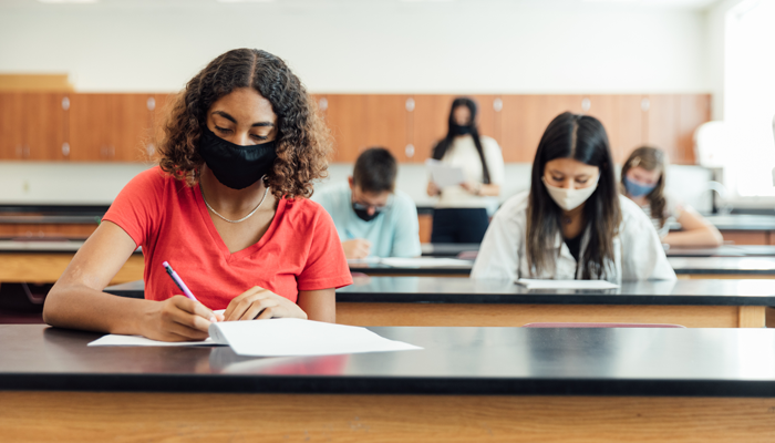 students sitting at desk writing a test with masks on indicating conducting education verification checks