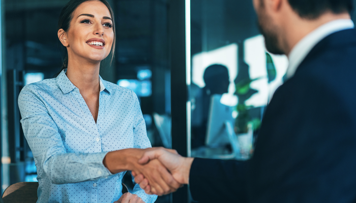 man in business suit facing a well dressed woman shaking hands accepting a job proposal