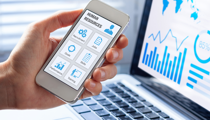 close up of hand holding smartphone with a human resource app and laptop open in background showing reporting