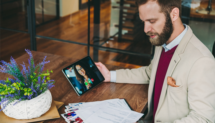 professional man looking over resumes and holding a table in right hand with a woman on the screen