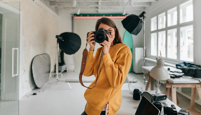 young woman photographer in studio holding camera to face about to take photo