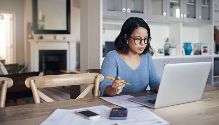 woman with glasses sitting in a home office with pencil in hand looking intently over background checks for remote employees on laptop screen