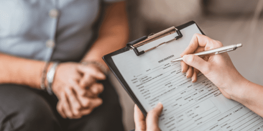 image of 2 people interviewing no faces, one holding a clipboard and pen completing an application