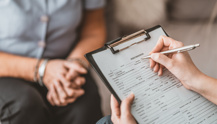 image of 2 people interviewing no faces, one holding a clipboard and pen completing an application