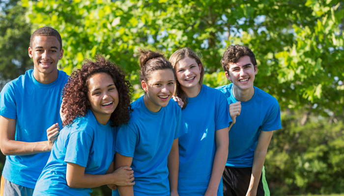 5 young camp counselors in a huddled group smiling showcasing importance of background checks for summer camp counselors