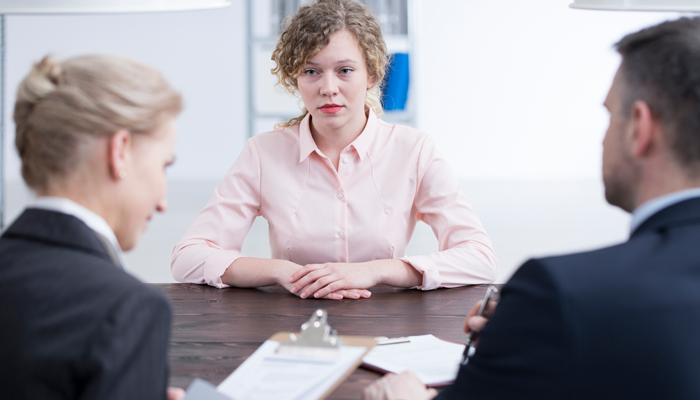 2 executives conducting an interview with a young women wearing a pink blouse who has nervous look on face