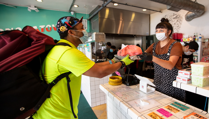 young man with mask and backpack ordering food at a takeout counter