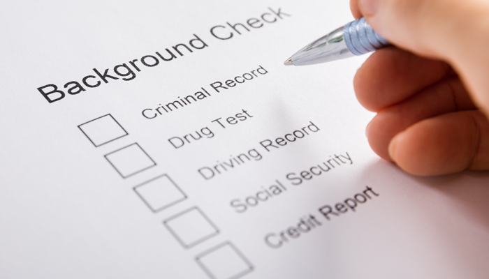 image of hand holding a pen to a background check application for rescreening employees