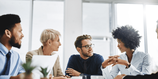 group of diverse professionals sitting around a desk conversing about the difference between pre and post employment screening