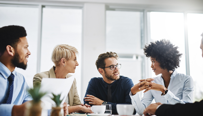 group of diverse professionals sitting around a desk conversing about the difference between pre and post employment screening
