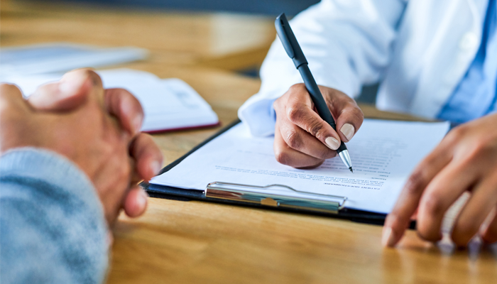 close up of 2 sets of hands, one with hands clasped and the other hr professional employee rescreening with a clipboard and application looking to review it.