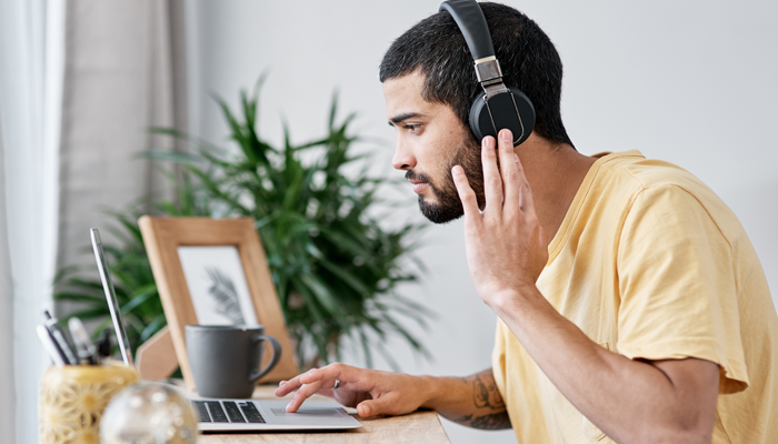 young man sitting at desk looking intently at laptop with headphones on indicating he's looking into skill development programs