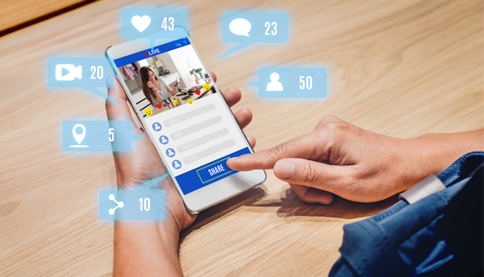 image of hands holding mobile phone with a social app showing his finger about to share and floating social bubbles surrounding the phone