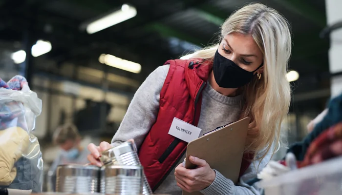 young blonde woman with mask wearing a volunteer tag holding a clip board and looking at a stack of aluminum cans