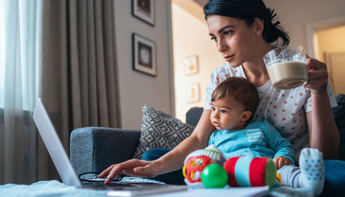 young woman with coffee in hand and baby on her lap looking at a laptop