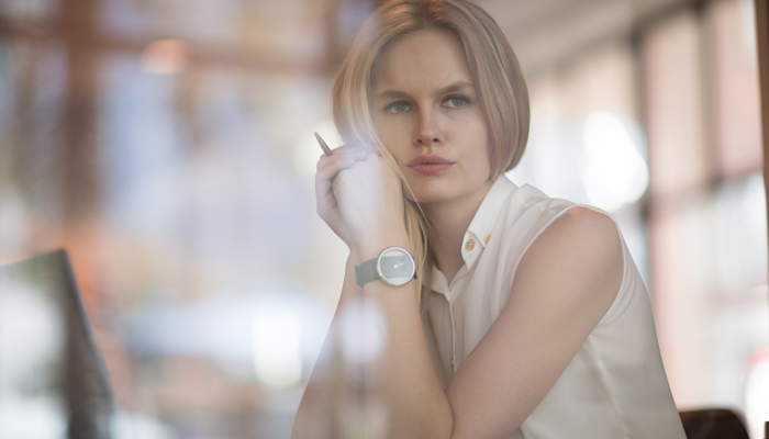 pretty woman sitting at desk holding a pen and hands to her check while looking out window in despair showcasing massive termination due to vaccination policy