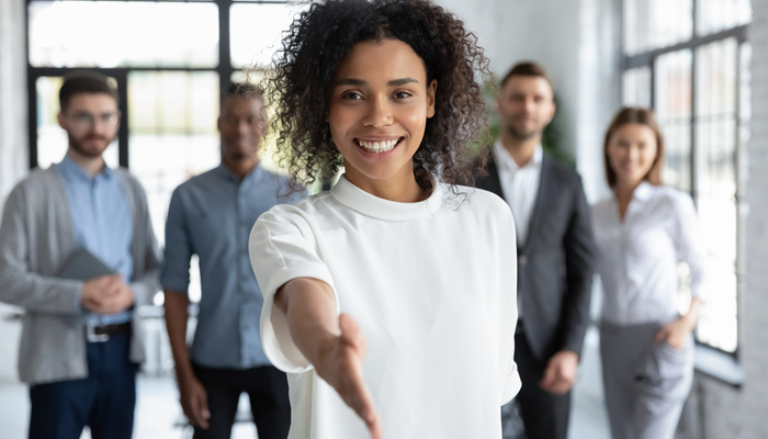 young smiling woman extending her hand for a handshake and 4 blurred young professionals standing behind her to indicate the job opportunities in Toronto