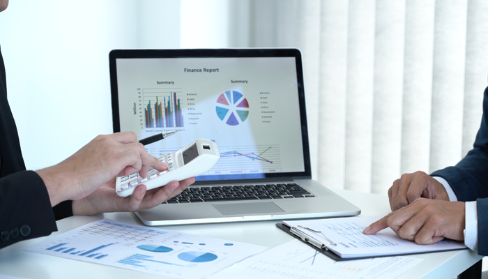 image of laptop with finance report on it and 2 professionals with clipboard and calculator discussing the credit check verifications