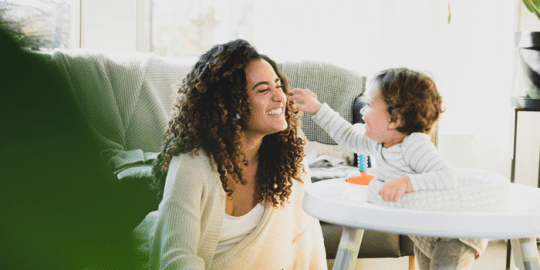 young woman smiling and laughing with a toddler indicating she is a sitter who has passed a criminal background check and is safely watching over the child