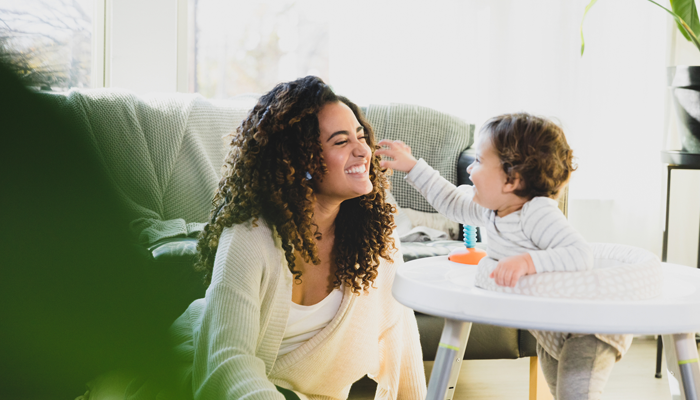 young woman smiling and laughing with a toddler indicating she is a sitter who has passed a criminal background check and is safely watching over the child