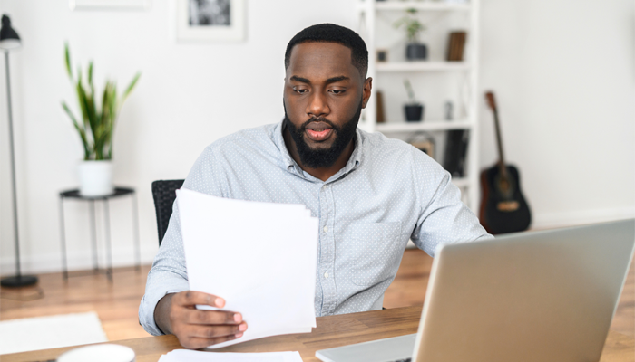 black man sitting at desk with laptop looking at resume