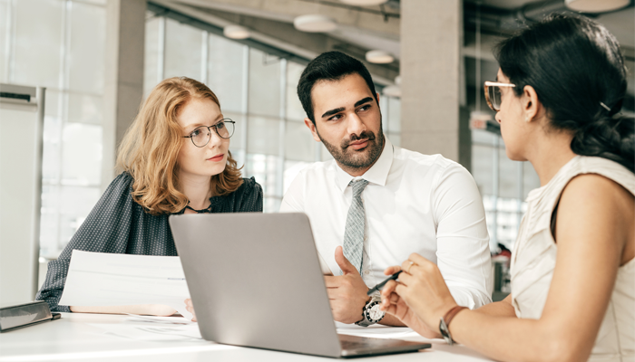 3 professionals in an office around a desk conversing about canadian background checks