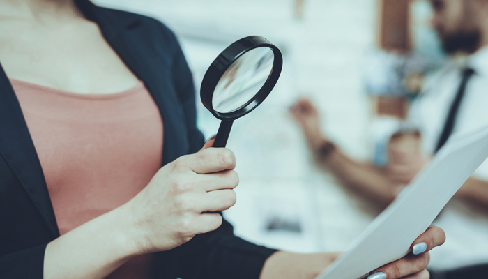 a human resource professional woman holding a magnifying class to a resume indicating a closer look at a criminal record check for employment