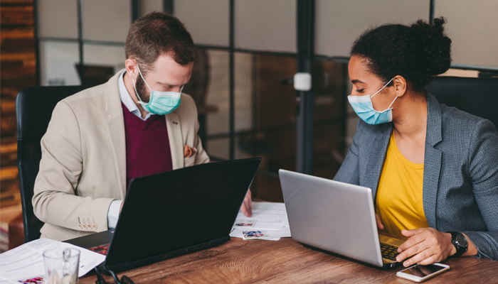 2 HR professionals sitting at desk in front of laptops with mask on completing employment screenings