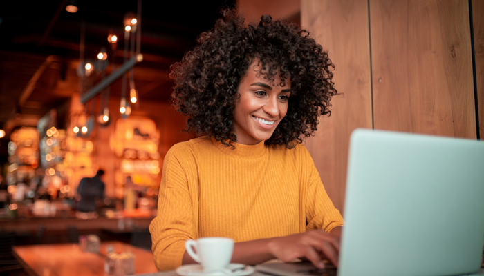 young woman sitting in a restaurant working at table smiling and working gig work on laptop