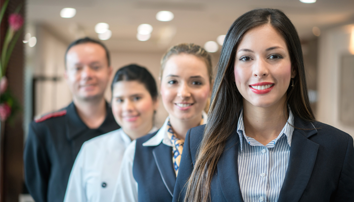 4 professionals smiling looking ahead with their hospitality jobs in uniform smiling at camera. One in focus and the rest not in focus