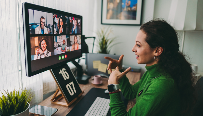 woman at home office wearing green sweater looking at big monitor with a 6 individuals on a zoom meeting discussing HR statistics
