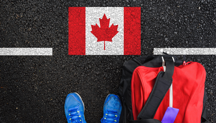 paved roadway with canadian flag and the feet and bag of a person indicating jobs for newcomers in canada