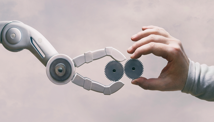 robotic hand and human hand each holding a cogwheel and bringing it together indicating automation in the workplace