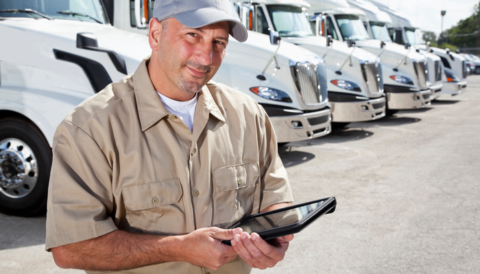 man standing with tablet in front of a line up of trucks in the supply chain and operations management industry