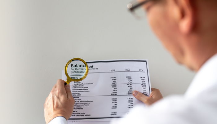 man holding a balance sheet with magnifying class looking closer at charity scams
