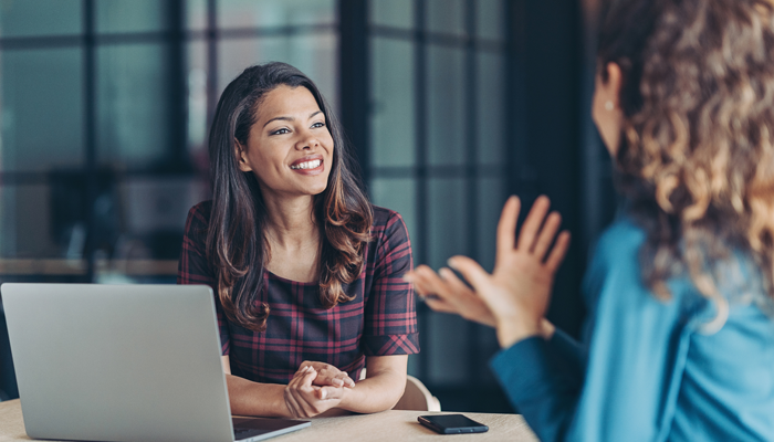 2 young professional women sitting around desk smiling having a conversation