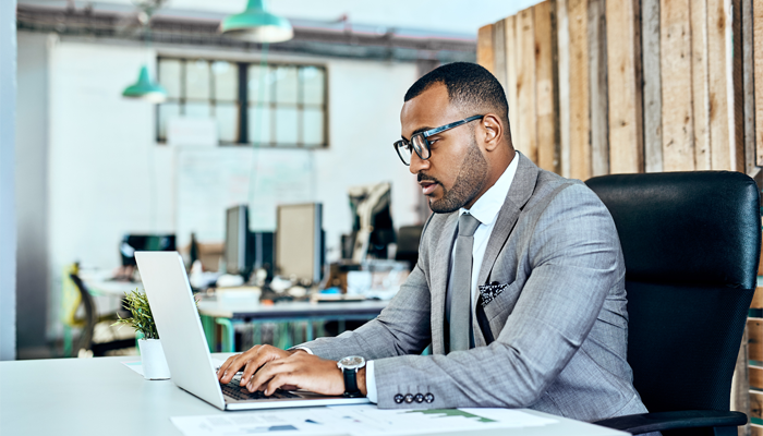 professional man in suit sitting at desk working on laptop completing social media screenings
