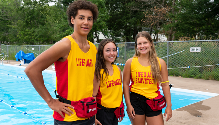 3 young lifeguards, one male and 2 female smiling at their summer jobs