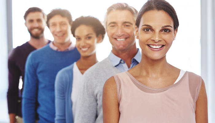 group of 5 smiling professionals in a row showing their return to the office