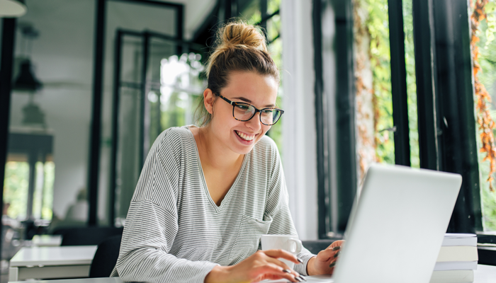 young woman with bun and glasses smiling looking at laptop starting work after completing a police background check
