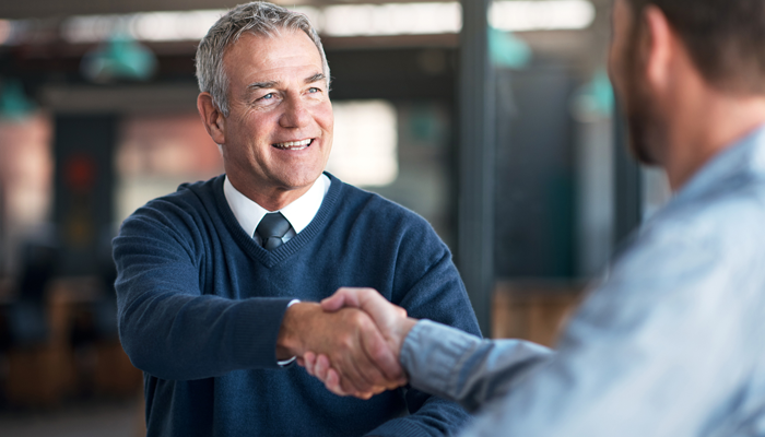 middle aged man with white hair in shirt and tie shaking the hand of another man showcasing the franchisor and franchisee partnership
