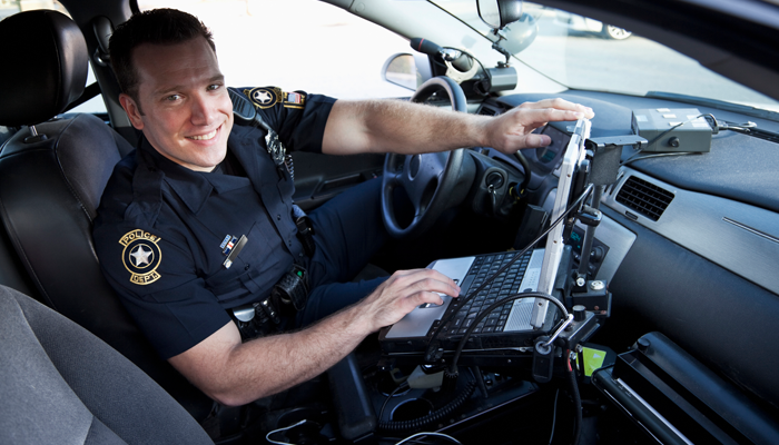 Police office in uniform sitting in car smiling using police technology