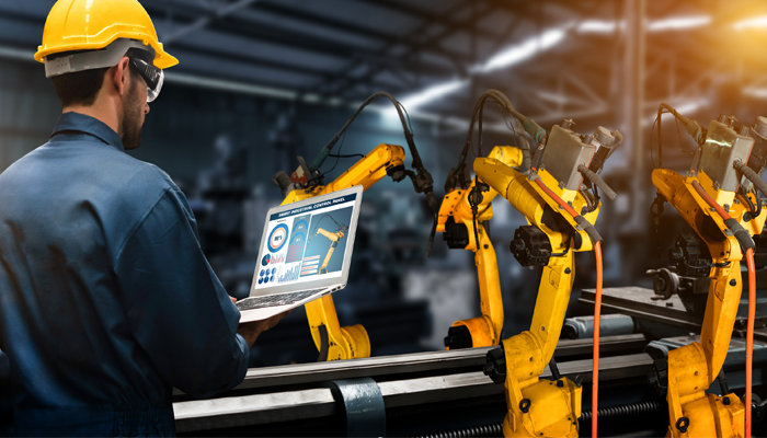 man in manufacturing warehouse wearing hard hat looking at reporting on laptop showcasing skill shortage in canada