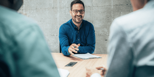 a smiling man with clipboard on desk in front of him and sitting across 2 men on other side of desk indicating autism in the workplace
