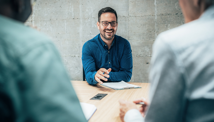 a smiling man with clipboard on desk in front of him and sitting across 2 men on other side of desk indicating autism in the workplace