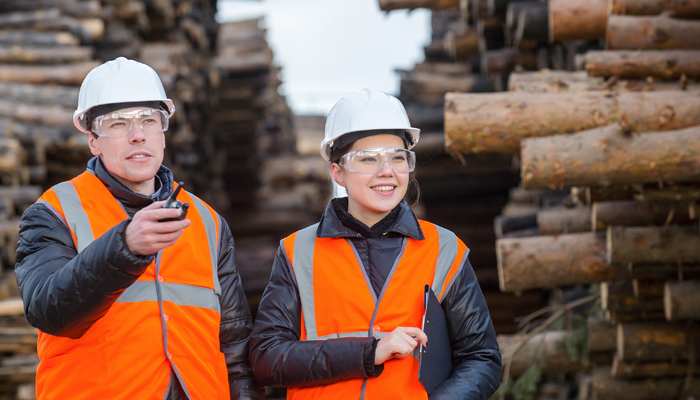 one male and one female worked wearing safety vest and hardhat standing in front of lumbar showcasing the skill shortage in canada