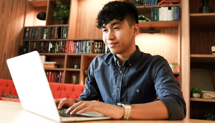 smiling young male sitting at home office desk typing on laptop