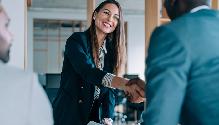 2 professionals shaking hands around a desk which seems to indicate a job interview
